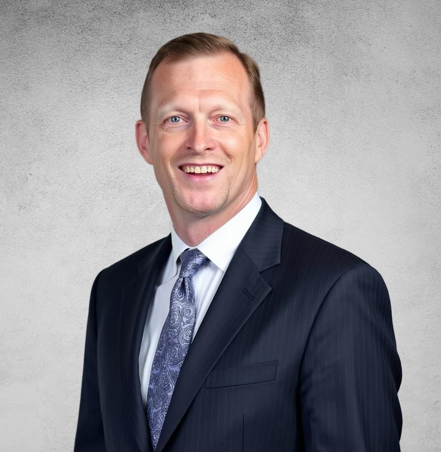 John Barlow, Senior Business Loan Consultant, smiles confidently in a dark suit and patterned tie. The background is a plain, textured gray surface.
